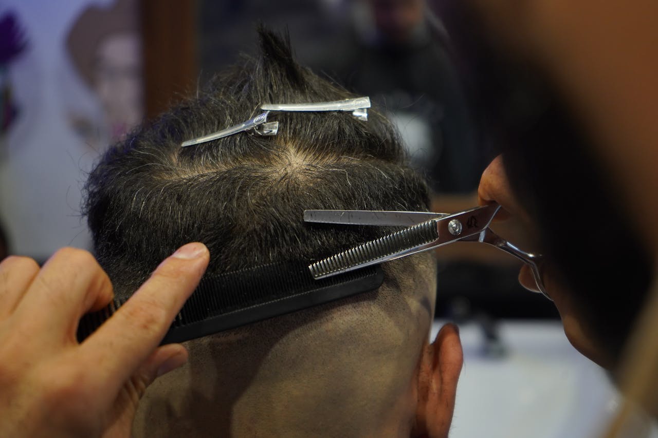 About Close-up of a barber skillfully cutting a customer's hair with scissors and a comb indoors.